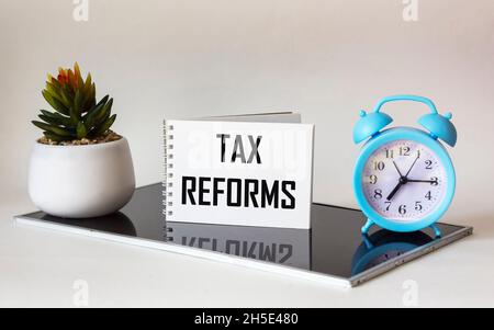 Clock, cactus and notebook on black glass board and white background with text - Tax reforms Stock Photo