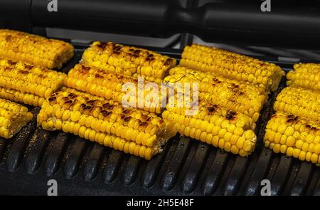 Close-up of slices of ready to eat grilled tasty yellow sweet corn cobs on black metal grill. Some brown seeds have slightly burnt surface. High angle Stock Photo