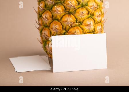 White paper business card with ripe pineapple on orange pastel background. Side view, copy space. Tropical, healthy food, vacation, holidays concept. Stock Photo