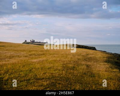 Walking from Crater to Dunstanburgh Castle 14th-century fortification in the summer coast landscape of Northumberland northern England UK Stock Photo