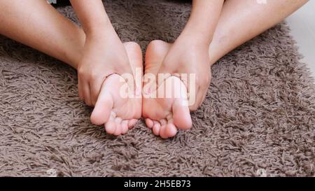 Woman sitting on the bed massages her feet, close-up.