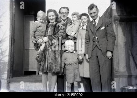 1940s, historical, friends and family, two men and their wifes with their young children standing together for a photo, England, UK. Both ladies wearng coats, with one of them in a fur coat and a gentleman in a three piece suit. Two small boys wearing matching sweaters. Stock Photo