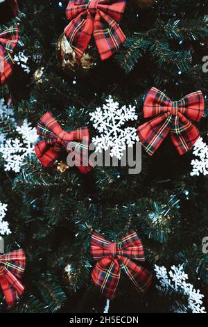 Red bows and white snowflakes hanging on the branches of a Christmas tree. Festive decor in interior. Stock Photo