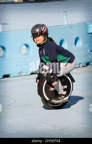 A young pre-teenage girl fearlessly rides on an Inmotion electric unicycle in Flushing Meadows Corona Par in queens, New York City. Stock Photo