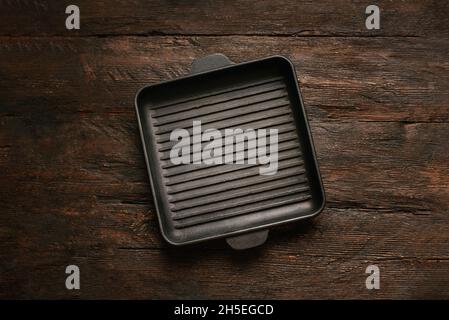 New empty cast-iron grill pan with two handles on wooden background. place for text. Flat lay top view black cast iron skillet for barbecue. Food Mockup Stock Photo