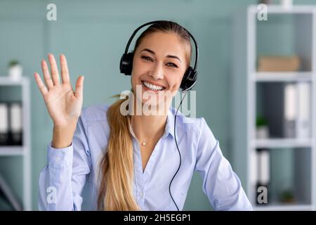 Virtual meeting. Happy businesswoman in headset making video call and waving hand wo webcamera Stock Photo