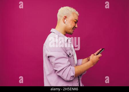 Fashionable young man browsing his favourite music playlists. Happy young man using a smartphone while wearing wireless earphones in a studio. Non-con Stock Photo