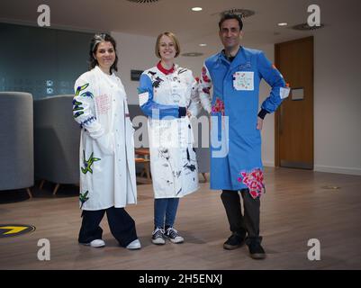 (left to right) Rosalind Wyatt, cancer patient Laura Nuttall and Professor Chris Jones wearing three lab coats which have been made into a 'wearable work of art', and are on display at the Institute of Cancer Research in Sutton, south west London. British textile artist Rosalind Wyatt has transformed three lab coats with hand-stitched quotes, letters and illustrations from children and adults with rare and hard to treat cancers, raising awareness of 'cancers of unmet need'. Picture date: Tuesday November 9, 2021. Stock Photo