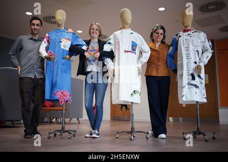 (left to right) Professor Chris Jones, cancer patient Laura Nuttall and Rosalind Wyatt pose next to three lab coats which have been made into a 'wearable work of art', and are on display at the Institute of Cancer Research in Sutton, south west London. British textile artist Rosalind Wyatt has transformed three lab coats with hand-stitched quotes, letters and illustrations from children and adults with rare and hard to treat cancers, raising awareness of 'cancers of unmet need'. Picture date: Tuesday November 9, 2021. Stock Photo