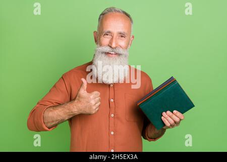 Photo of handsome senior man information novel show thumb-up good ad suggest isolated over green color background Stock Photo