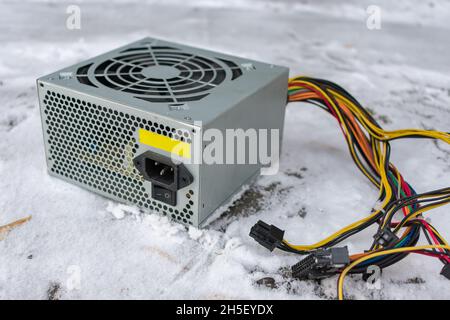 A computer power supply lies in a landfill in the snow in winter Stock Photo