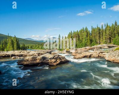 Beautiful landscape with long exposure water stream and cascade of river Kamajokk, boulders and spruce tree forest in Kvikkjokk village in Swedish Stock Photo