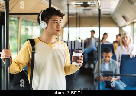 Focused asian guy listening music in bus drinking coffee Stock Photo