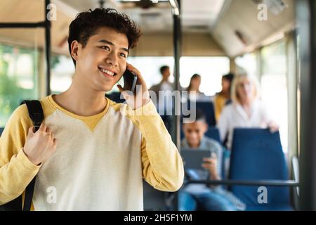 Smiling Asian guy taking bus, talking on cellphone Stock Photo