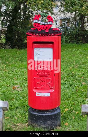 Felpham Village Post Box yarn bombed with crocheted Poppy Wreath bearing the lettering 'Lest We Forget' Stock Photo