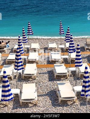 Parasols and deckchairs on beach of Nice in sunny summer day with blue sky, Nice, French Riviera, France Stock Photo