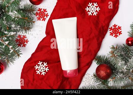 White cosmetic tube, a jar of cream on red background with fir tree and decorations, winter christmas body care products Stock Photo