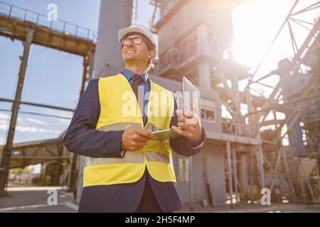 Joyful man with notebook standing outdoors at factory Stock Photo