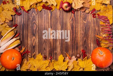 Autumn background with yellow maple leaves, pumpkins, red apples and berries. Frame of fall harvest on aged wood with copy space. Mockup for seasonal Stock Photo