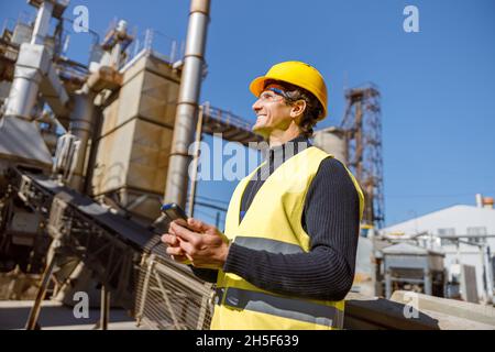 Cheerful man engineer using smartphone at industrial site Stock Photo