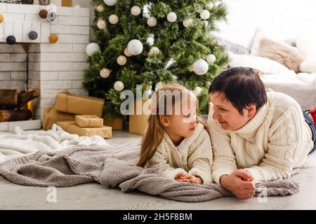 Mother and daughter unwrapping a present lying on the floor in the living room Stock Photo
