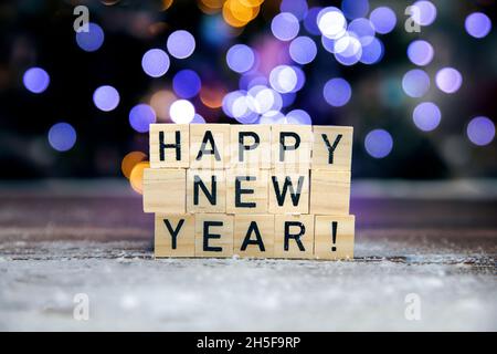 Bright text Happy New Year 2022 on bokeh background written with wooden cubes and snow, colorful festive design, Christmas, New Year, Holiday concept Stock Photo