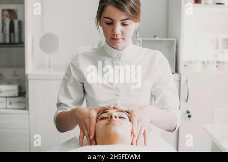 Beautician rubbing client forehead, making relaxing head massage in spa salon. Skin care concept Stock Photo