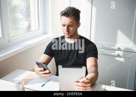 Businessman sitting at table and thinking at business plan. On table is laptop, tablet, smartphone, notebook. Remote work Stock Photo