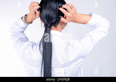 Back view photo of a woman in a white t-shirt with gold watch on her hand and the ring straightens long black tail. Stock Photo