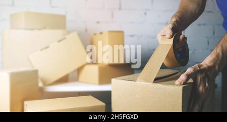 warehouse order picker packing and sealing cardboard box with tape for dispatch Stock Photo