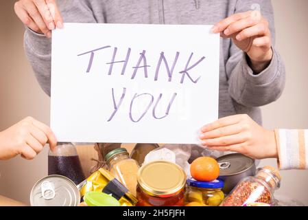 Thank you for donation. Volunteers holding paper sheet with message Thank you over food donation box full of grocery Stock Photo