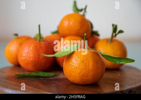 mandarine fruits with leaves lying on wooden surface. Selective focus on foreground fruit Stock Photo