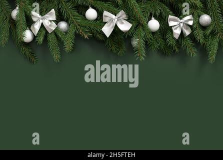 Christmas decorations with silver bows and baubles on a green background. Christmas border. Happy New Year. Space for text. Top view, flat lay. Stock Photo