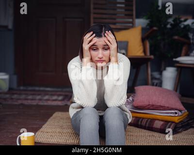 Young depressed asian woman sitting on porch of backyard. She feeling sad and worried suffering depression in mental health. Mental health, anxiety depressed thinking chinese lady. Stock Photo