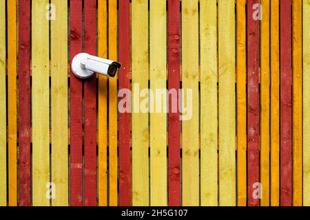 white surveillance camera on the wall of yellow and red painted boards Stock Photo