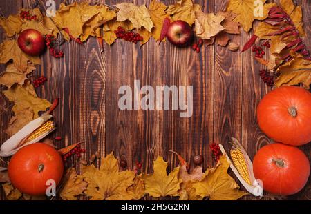 Autumn background with yellow maple leaves, pumpkins, red apples and berries. Frame of fall harvest on aged wood with copy space. Mockup for seasonal Stock Photo