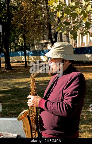 Dnepropetrovsk, Ukraine - 09.17.2021: A man plays the saxophone in the park. Street musician with saxophone performing music for charity. Public solo Stock Photo