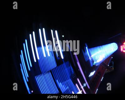 Abstract pattern of white & blue lights in the night sky from a spinning white knuckle fairground ride at the funfair. Stock Photo