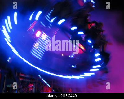 Circular pattern of white line light trails in the night sky, caused by a spinning fairground ride that almost looks like an alien sci-fi spacecraft. Stock Photo