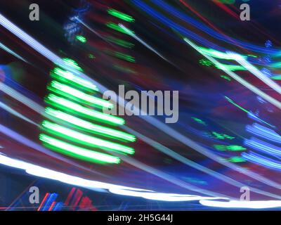 Abstract pattern of green, blue & red lights creating lines in the night sky as an illuminated rotating fairground ride spins very fast. Stock Photo