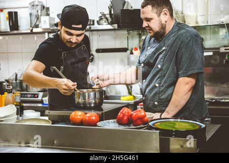 two chefs in the restaurant kitchen are trying food. training Stock Photo