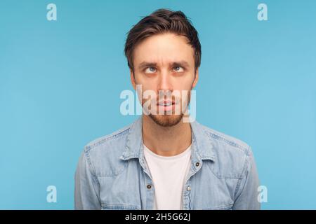Portrait of comic positive handsome man wearing denim shirt, looking cross-eyed, having fun with silly face expression, playing fool. Indoor studio shot isolated on blue background. Stock Photo