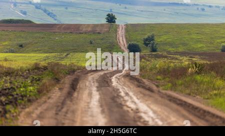 Country road through green fields, hills extending into the distance beyond the horizon Stock Photo