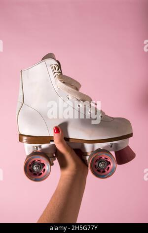 Woman hand holding a white double row roller skates with a pink background Stock Photo