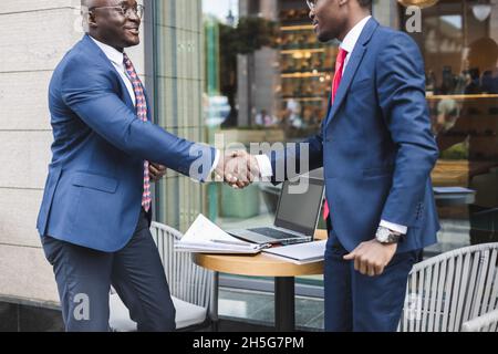 Portrait of two black African American businessmen in suits shaking hands outdoors. The joy of meeting good friends Stock Photo