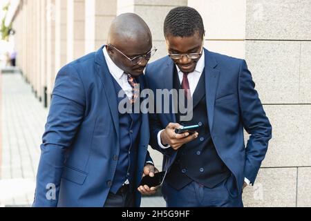 Two black African American businessmen friends in suits are talking while standing on the street. Outdoor business meeting Stock Photo