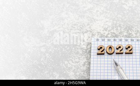 Notebook and pen on the grey. Wooden numbers date 2022. A blank sheet of paper and a white pen. Stock Photo