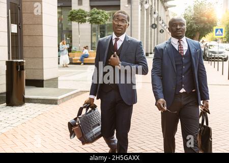 Two dark-skinned african american businessmen in suits with briefcases walk along the city street Stock Photo