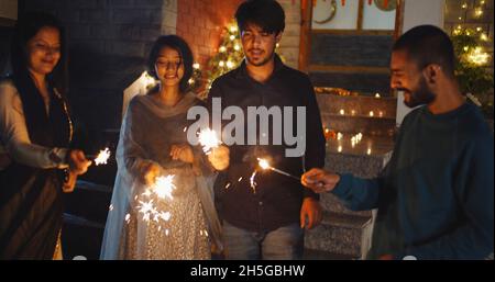 Group of  friends celebrating something with sparklers outdoors in front of a decorated house Stock Photo