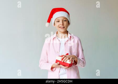 Smiling funny guy in red santa hat holding a christmas present in his hand. Christmas concept. Caucasian teenager on background happy and joyful Stock Photo
